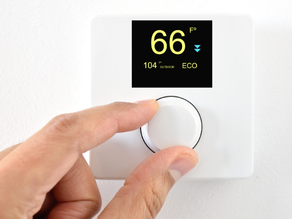 This image shows someone adjusting a white, digital thermostat in their home. Making small adjustments, like to the thermostat, is a great way to begin a frugal living lifestyle.